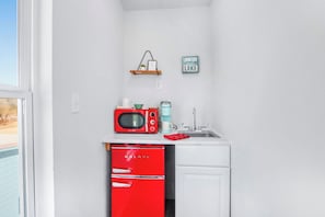 Eine kompakte Küche mit einer roten Mikrowelle, einer Kaffeemaschine, einem Spülbecken und einem kleinen Kühlschrank.