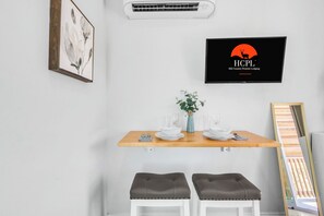 A dining area with a wooden table, two cushioned stools, a vase with a plant, and a television displaying 'HCPL Hill Country Premier Lodging'. - Private Deck & Hill Country Lake Views (Canyon Lake)