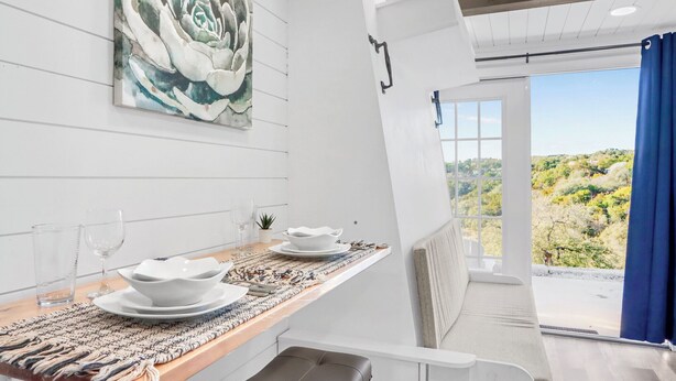 A dining area with a table set for two, a painting on the wall, and a view of greenery outside. - Canyon Lake Container Retreat w/ Views (Canyon Lake)