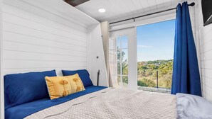 A bedroom with a bed, a view through a window, and a curtain. - Canyon Lake Container Retreat w/ Views (Canyon Lake)