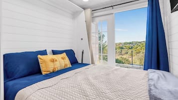 A bedroom with a bed, a view through a window, and a curtain.