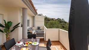 A balcony with a dining table set for a meal, outdoor seating, and a view of the surrounding landscape. - Apartment in Elviria With Terrace, Marbella (Marbella)