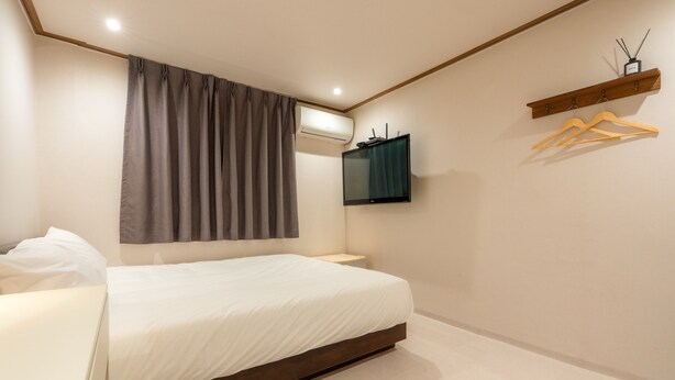A bedroom with a bed, a TV mounted on the wall, a wooden shelf with hangers, and a wall-mounted air conditioner. - STAYV Jang-an (Seoul)