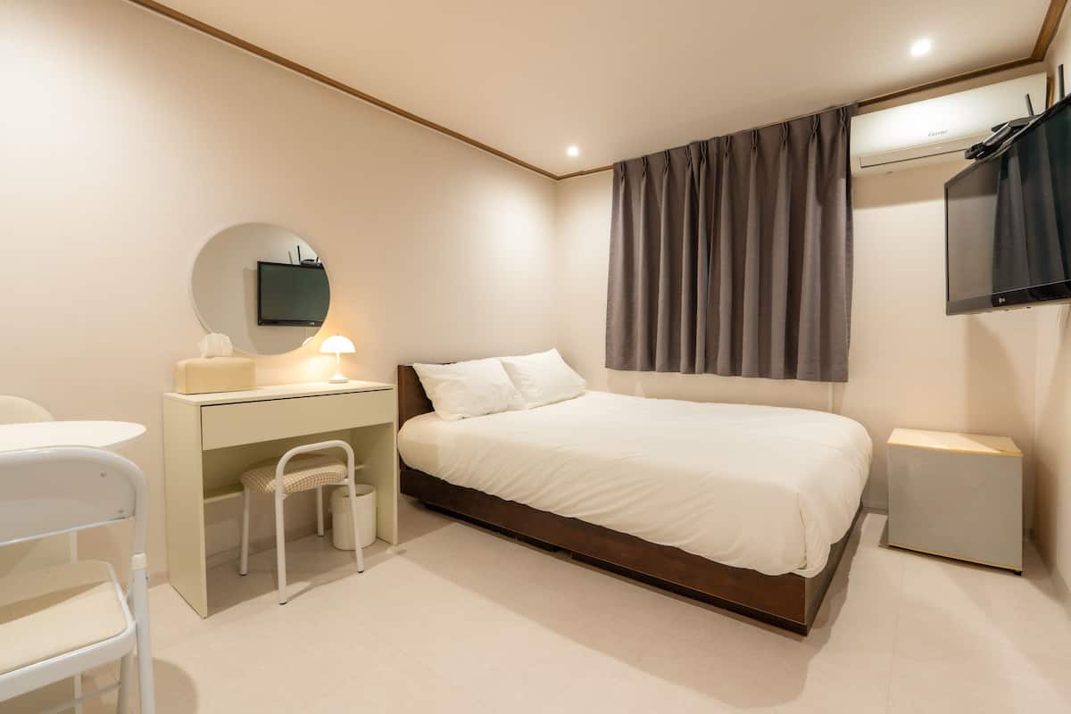A modern bedroom with a bed, desk, chair, and a mounted TV.