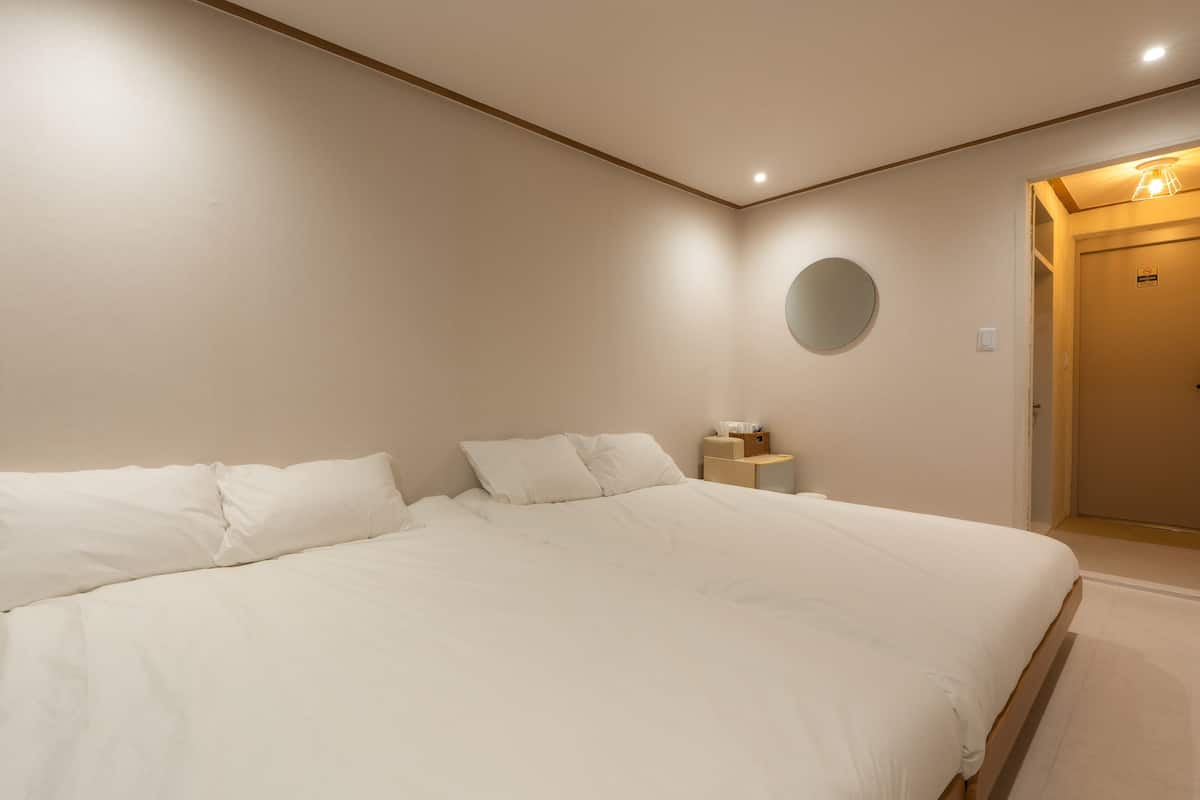 A bedroom with a large bed, a bedside table, a round mirror, and a door.