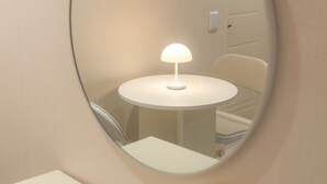 A round mirror on a wall, reflecting a table with a lamp, a chair, and a tissue box. - STAYV Jang-an (Seoul)