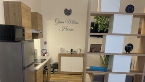 A modern kitchen with a refrigerator, microwave, and coffee maker. There is a small dining area with a table and chairs. The room has a wooden floor and a bed with a white comforter. - Nice newly renovated apartment with all amenities near the metro. (Milano)