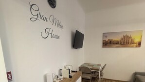 A room with a wooden floor, a desk with a chair, a flat-screen TV mounted on the wall, and a painting of a cityscape. - Nice newly renovated apartment with all amenities near the metro. (Milano)