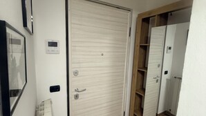 A hallway with a wooden floor, a white door with a handle, a thermostat, and a framed picture on the wall. - Nice newly renovated apartment with all amenities near the metro. (Milano)