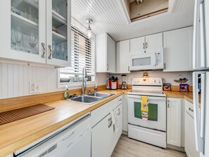 Eine kompakte Küche mit weißen Schränken, einer Mikrowelle, einem Backofen, einem Spülbecken und einem Fenster mit Jalousien.