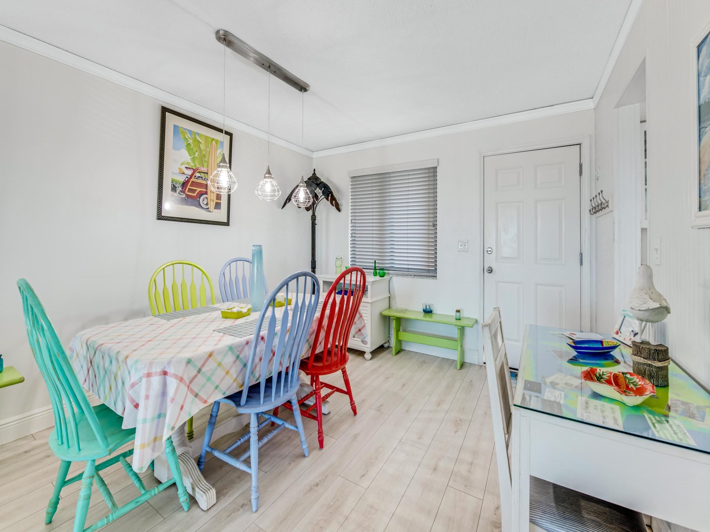 Un coin repas avec une table dressée pour quatre personnes, des chaises colorées, un banc et une petite table sur laquelle se trouvent un bol et une lampe.