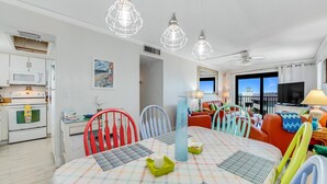 Ett ljust vardagsrum med matplats, vita väggar, en tv och en balkong med utsikt.