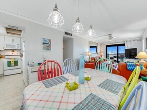 Ein helles Wohnzimmer mit Essbereich, weißen Wänden, einem Fernseher und einem Balkon mit Aussicht.