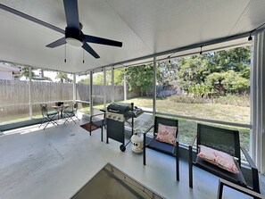 A covered patio with a ceiling fan, a grill, outdoor furniture, and a view of a backyard. - Starfish House | Pet-Friendly + Extended Stays (Ormond Beach)
