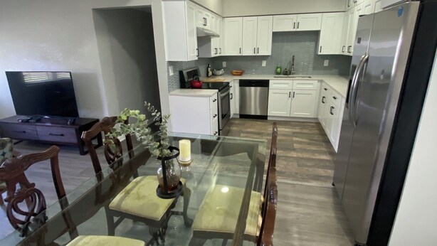 Una cocina moderna con armarios blancos, un refrigerador de acero inoxidable y una mesa de comedor de vidrio con sillas.