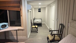 Un dormitorio con una cama, una silla, una mesa con microondas y una ventana con persianas.