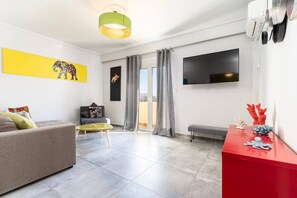 A modern living room with a sofa, a glass coffee table, a red side table, a flat-screen TV, and a yellow artwork on the wall. - Evergreen Loft | Modern City Centre Living (Kos)