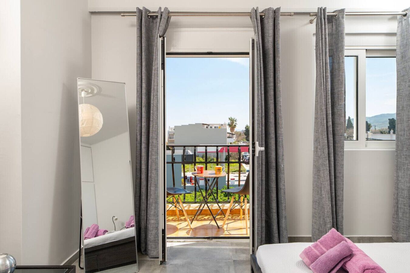 Een hotelkamer met een bed, nachtkastje, spiegel en balkon met tafel en stoelen.