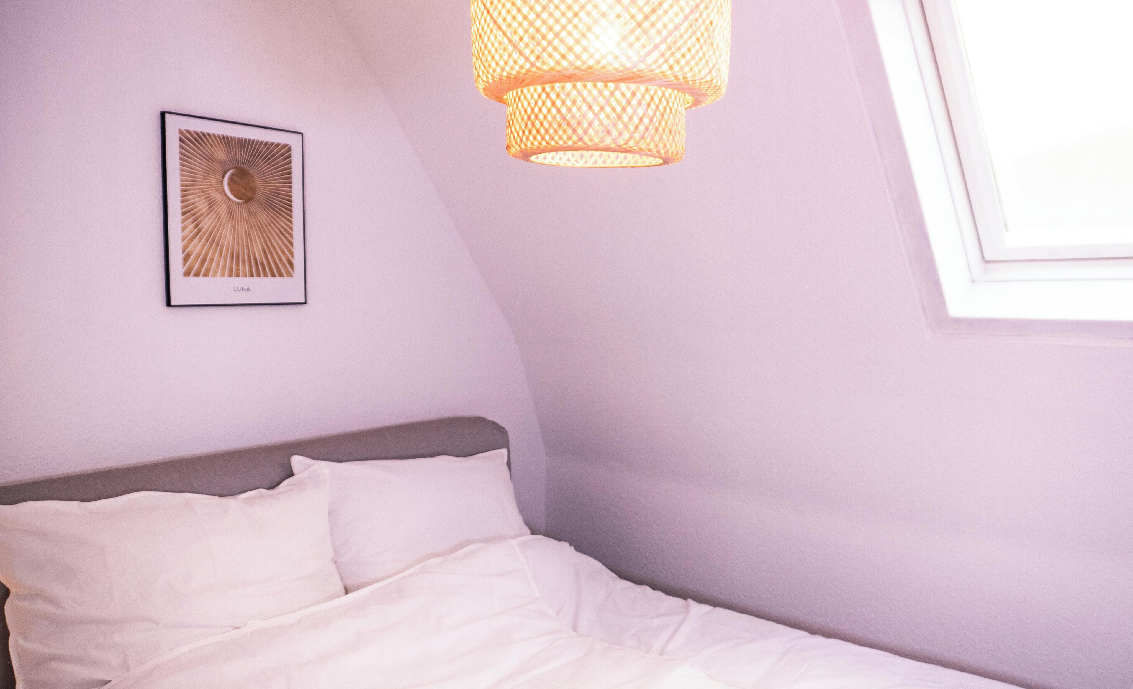 Ein Bett mit weißer Bettwäsche, ein an der Wand befestigter Bilderrahmen und eine Pendelleuchte.