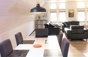 A modern living room with a dining area, featuring a large table, sofas, and a hanging light fixture. - Stylish apartment - Between the gates (Bad Münstereifel)