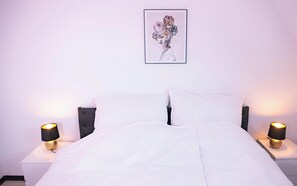 A neatly made bed with white linens, two bedside lamps with black shades, and a framed artwork on the wall.
