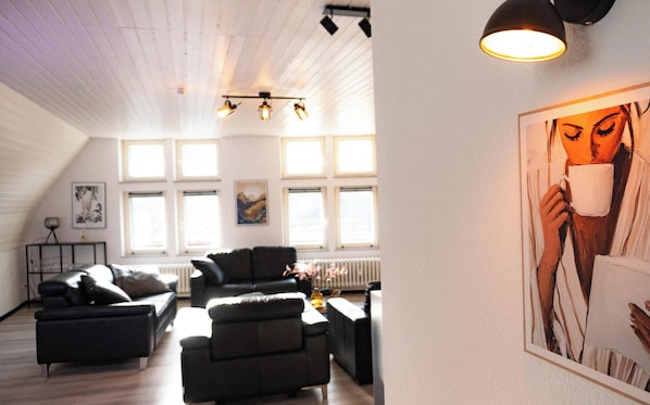A spacious living area with a high ceiling, multiple windows, and a large painting on the wall.