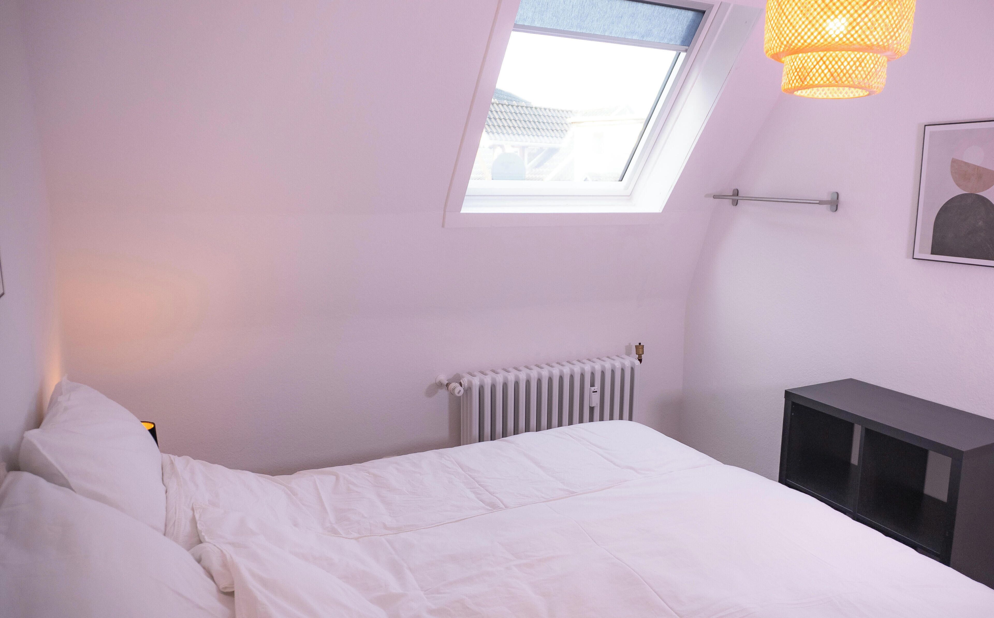 Een slaapkamer met een bed, radiator, raam en bureau.