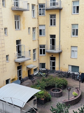 Ein mehrstöckiges, gelbes Gebäude mit Balkonen, einem Innenhof mit Blumentöpfen und Fahrrädern vor der Tür.