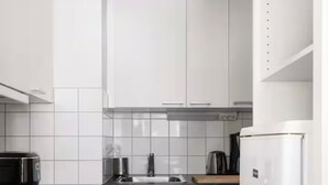 A compact kitchen with white cabinets, a black countertop, a microwave, a kettle, and a refrigerator. - Peaceful Artsy Home Stay (Helsinki)