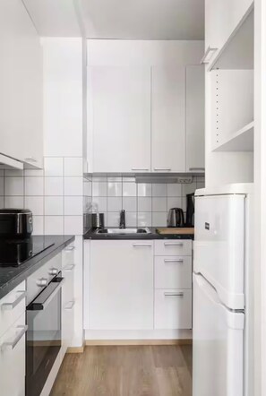 Eine kompakte Küche mit weißen Schränken, einer schwarzen Arbeitsplatte, einer Mikrowelle, einem Wasserkocher und einem Kühlschrank.