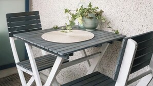 A small outdoor table with a woven placemat, surrounded by two chairs, against a textured wall with a blue trim. - Peaceful Artsy Home Stay (Helsinki)