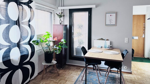 A dining area with a table, chairs, a potted plant, and a window with blinds. - Peaceful Artsy Home Stay (Helsinki)