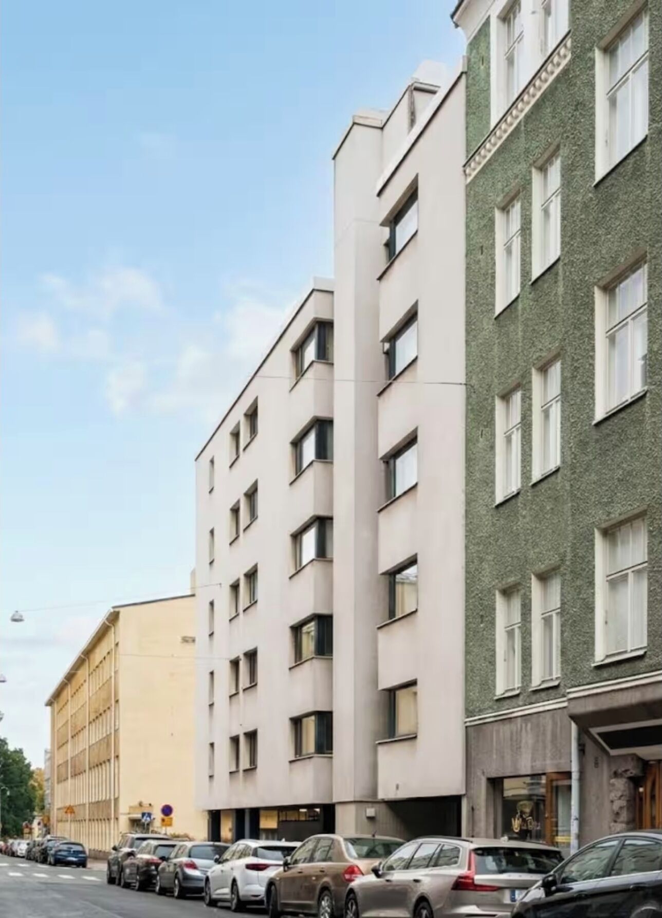 En bygning med flere etager og en række parkerede biler foran.
