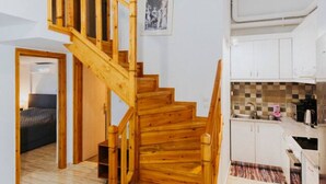 Una escalera de madera que lleva a un dormitorio, una cocina con armarios blancos y suelo de baldosas.