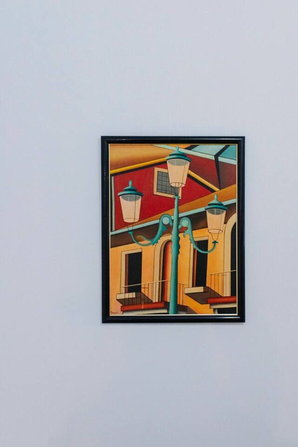 A framed artwork of a building with a red facade, a green street lamp, and a window.