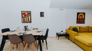 Un comedor con una mesa preparada para cuatro personas, un sofá amarillo y dos cuadros en las paredes.