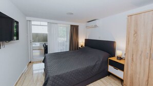 Un dormitorio con cama, armario, televisor, mesita de noche con lámpara y puerta corrediza a un balcón.