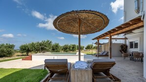 Ein Poolbereich mit Liegestühlen, einem Holztisch und einem Strohdachschirm.
