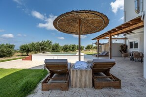 Un espace aménagé au bord de la piscine, avec des chaises longues, une table en bois et un parasol en chaume.