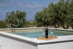 Une piscine, une bouteille de vin et deux verres sur un plateau en bois.