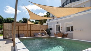 En pool med solstolar, ett trästaket och en byggnad med vita väggar och en balkong.