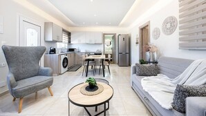 En modern lägenhet med en grå soffa, en grå fåtölj, en matplats, ett kök och ett vardagsrum.