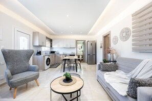 Um apartamento moderno com sofá cinzento, poltrona cinzenta, área de jantar, cozinha e sala de estar.