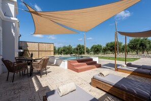 Ein Poolbereich mit Tisch und Stühlen, Sonnenschirm und Blick auf Pool und Grünfläche.