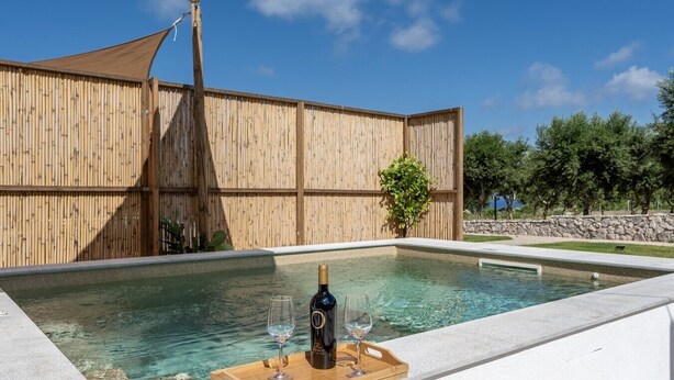 Ein Pool mit Holzterrasse, eine Weinflasche und zwei Gläser auf einem Tablett.