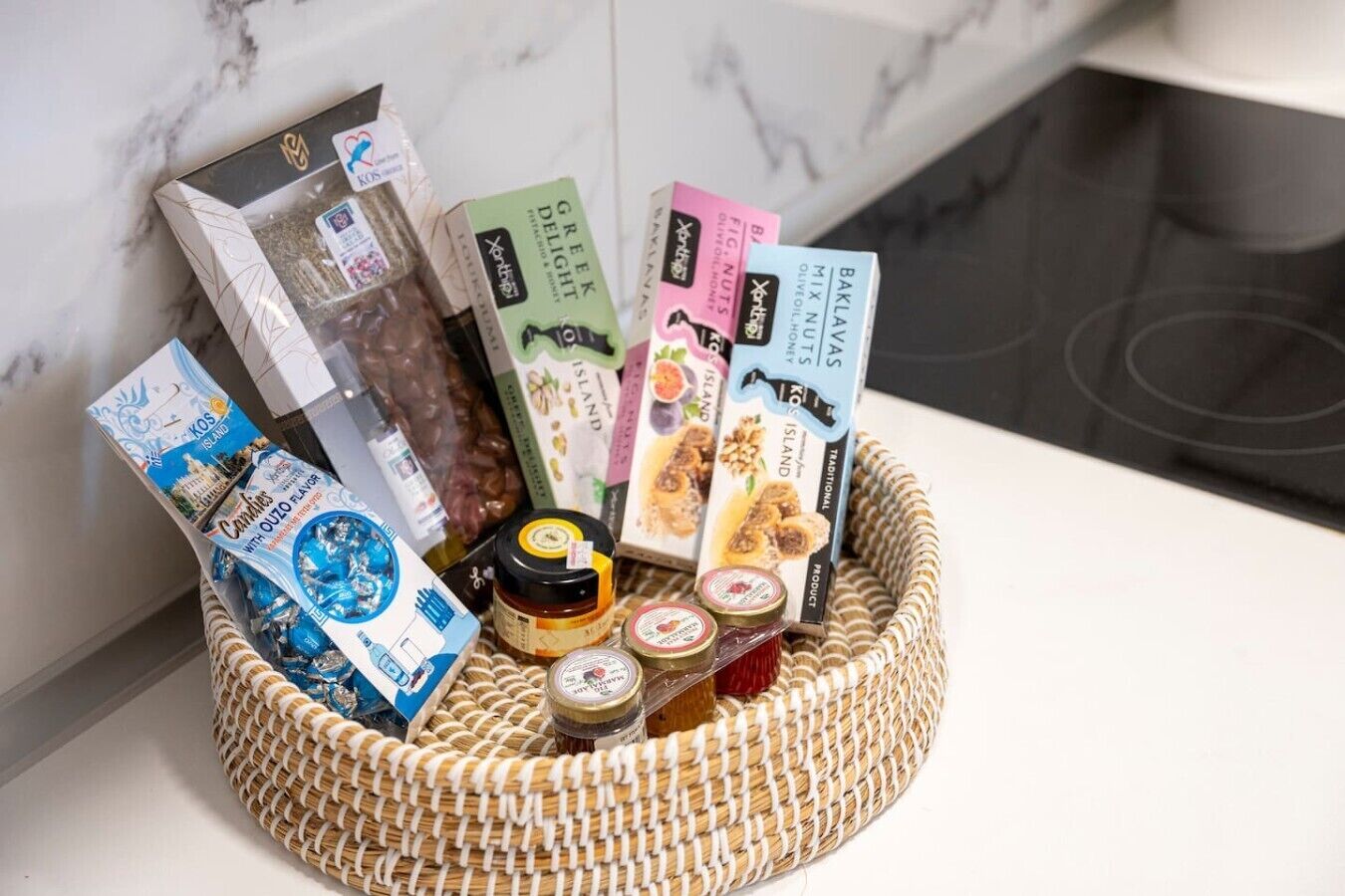 A wicker basket filled with various food items and packaged goods, placed on a marble countertop.