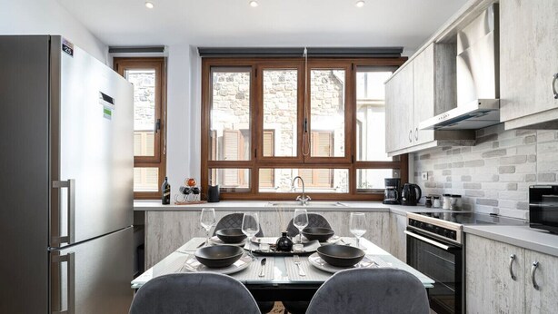 Cozinha moderna com mesa de jantar para dois, forno embutido e uma janela grande com persianas de madeira.
