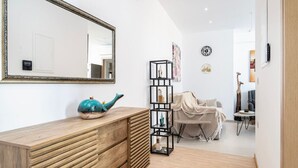 Uma sala de estar moderna com cômoda de madeira, uma estante preta alta, um espelho grande e uma área de estar aconchegante com um cobertor.