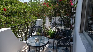 A balcony with a glass table and chairs, surrounded by greenery and red flowers. - Thines Studios : Studio B (Kampos)