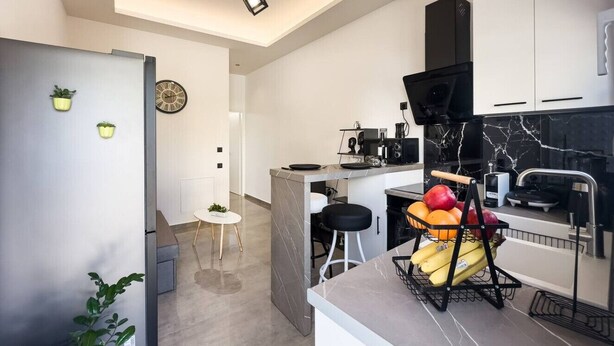 Une cuisine moderne avec un plan de travail en marbre, une hotte noire et un panier de fruits posé sur le plan de travail.